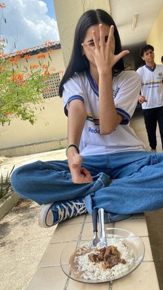 a woman sitting on the ground with her hand up to her face while eating food