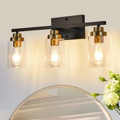 three light bathroom fixture with clear glass shades and brass accents, on a white wall