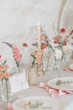 the table is set with pink and orange flowers in glass vases, plates, and candles