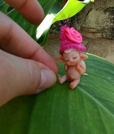 a small toy doll sitting on top of a green leaf