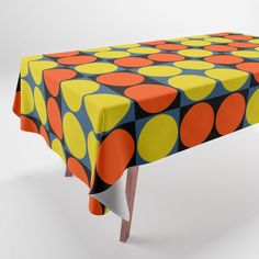 an orange, yellow and blue polka dot tablecloth on a wooden stand with white legs