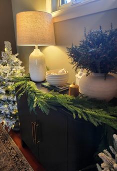 a table with christmas decorations on it and a lamp next to the sideboard in front