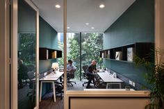 two people sitting at desks in an office with glass walls and large sliding doors