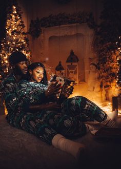 a man and woman sitting next to each other in front of a christmas tree with lights