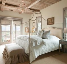 a bedroom with a canopy bed and chandelier in front of two windows that look out onto the water