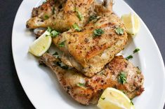 two pieces of chicken on a white plate with lemon wedges