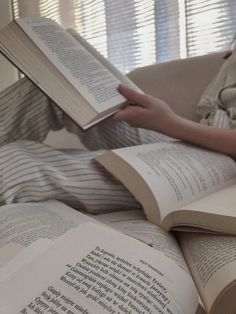 a person laying down reading a book on top of a couch next to a window