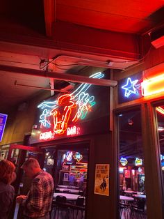 people are standing in front of a restaurant with neon signs on the walls and ceiling