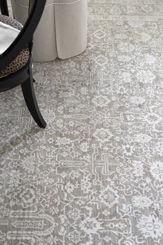 a white and gray rug with an ornate design on the floor next to a chair