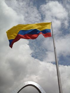 a large flag flying in the wind next to a tall metal structure with a sculpture behind it