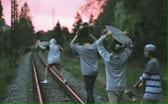 three people standing on train tracks with their backs to the camera, one holding a skateboard over his head