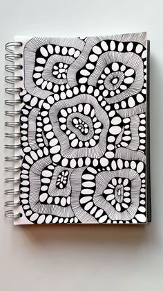 a black and white drawing on top of a spiral notebook with an intricate design in the middle