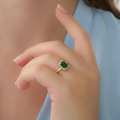 a close up of a person wearing a ring with a green stone on the middle