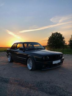 a black car parked on top of a parking lot next to a field at sunset