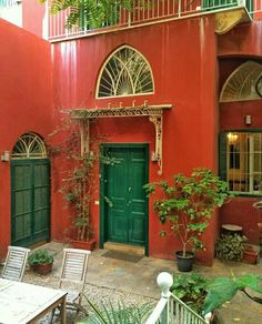 a red building with green doors and tables in front of it's windows, surrounded by greenery