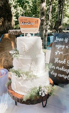 a three tiered wedding cake sitting on top of a wooden table next to a sign