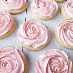 pink frosted rose cookies sitting on top of a white wooden table next to each other