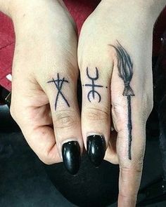 two people with tattoos on their fingers holding each other's hands and pointing to the left