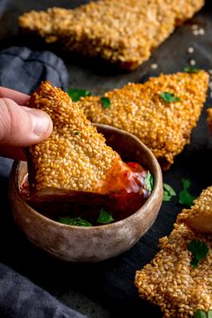 someone dipping some kind of food into a small bowl with other foods in the background