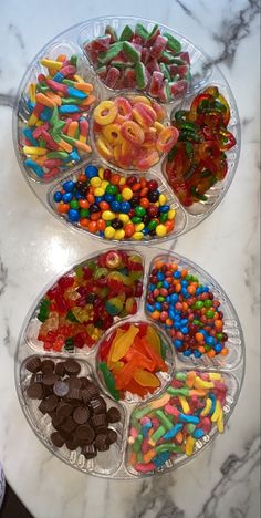 three plastic trays filled with different types of candies on a marble counter top