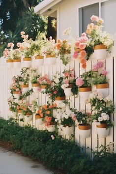 many potted flowers are on the side of a white picketed - off fence