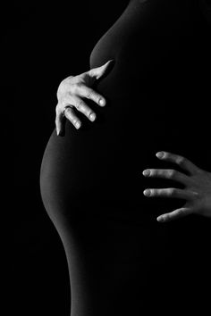 black and white photograph of a pregnant woman's stomach with her hands on the belly