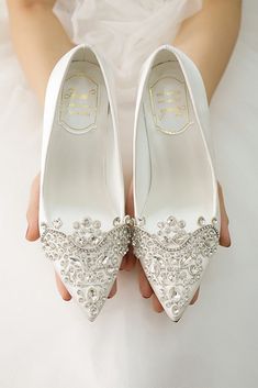 a bride holding her wedding shoes in front of her face and the bottom of her dress