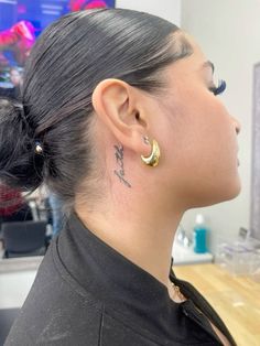 a woman with a tattoo on her neck and behind her ear is looking at the camera