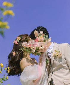 a bride and groom kissing in front of yellow flowers on a sunny day with blue sky behind them