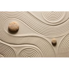 two rocks sitting on top of a sandy beach next to waves and circles in the sand