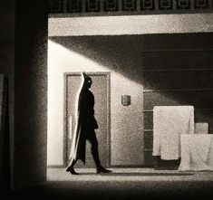 black and white photograph of a person walking in an empty room with curtains on the wall