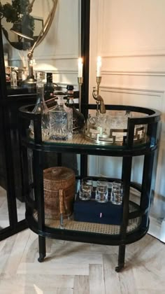 a glass table with bottles and glasses on it in front of a mirror, next to a candle