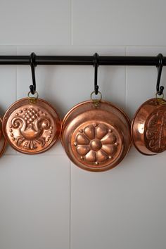 four copper pans hanging on a black rack