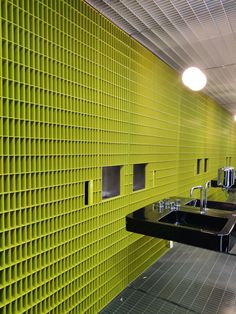 two sinks in a public restroom with yellow walls and green tiles on the wall behind them