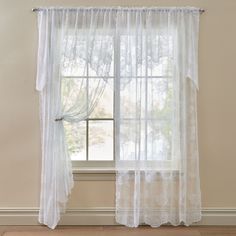 a window with white sheer curtains in front of a beige wall and hardwood flooring