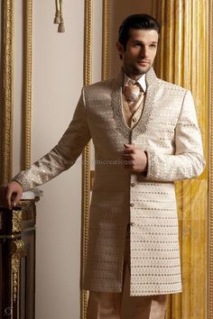 a man in a suit and tie standing next to a gold wallpapered room