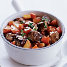 a white bowl filled with meat and vegetables on top of a table next to a fork