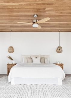 a white bed sitting under a ceiling fan in a bedroom next to a wooden headboard