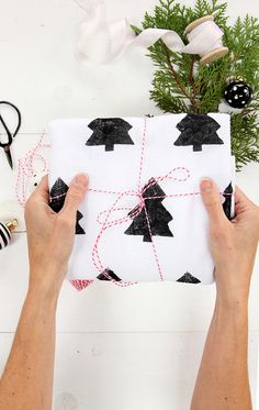 two hands holding a wrapped present on top of a white table next to christmas decorations