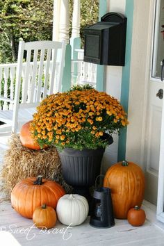 pumpkins and gourds are sitting on the front porch with hay bales