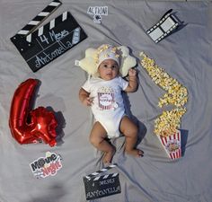 a baby laying on top of a blanket next to some balloons and movie signs in front of them