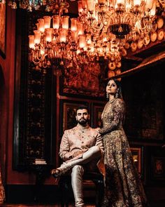 a man and woman standing in front of a chandelier with lights hanging from the ceiling