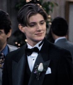 the young man is wearing a tuxedo and standing in front of other men