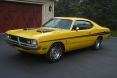 a yellow muscle car parked in front of a garage with a red door behind it