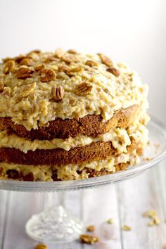 a stack of cake sitting on top of a glass plate covered in frosting and nuts