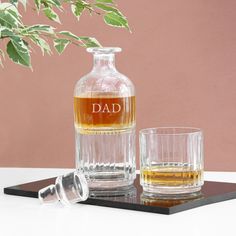 two glasses and a decanter sitting on a table next to a vase with leaves