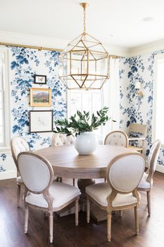 the dining room table is surrounded by white chairs and blue wallpaper with flowers on it