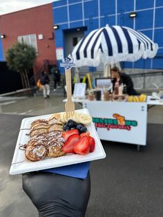 a person holding up a plate of food with strawberries and bananas on it in front of a blue building