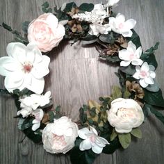 a wreath made out of flowers and leaves on a wooden surface with the center surrounded by greenery