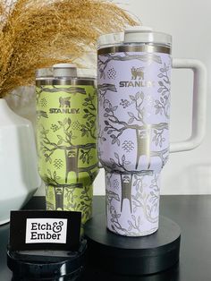 two travel mugs sitting next to each other on top of a black countertop